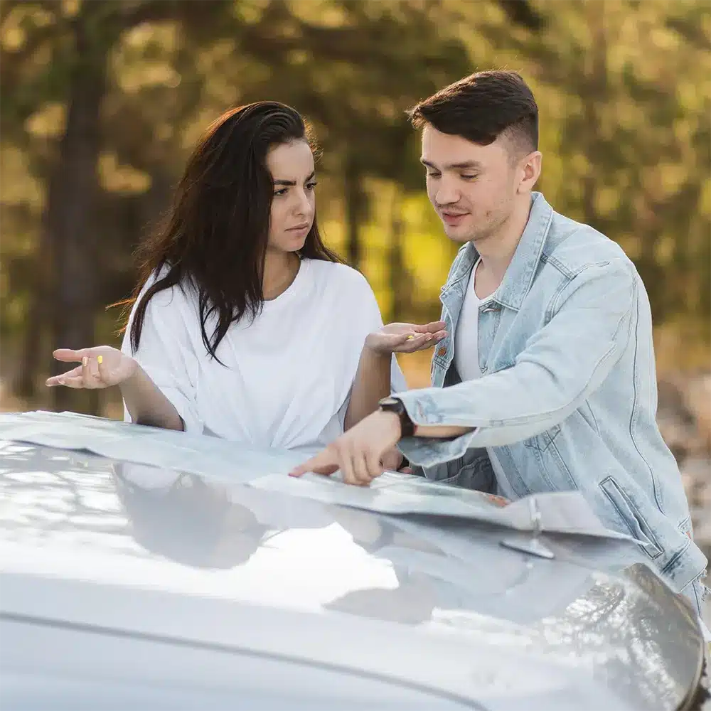 Concerned couple reviewing paperwork on a car hood, representing the frustration of dealing with a defective vehicle.