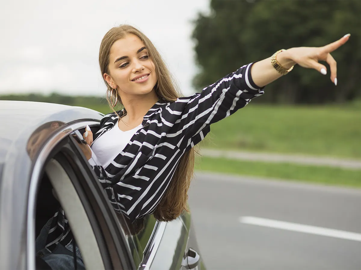 Woman leaning out of a car window and pointing, symbolizing confidence and a clear path forward after resolving a Lemon Law case.