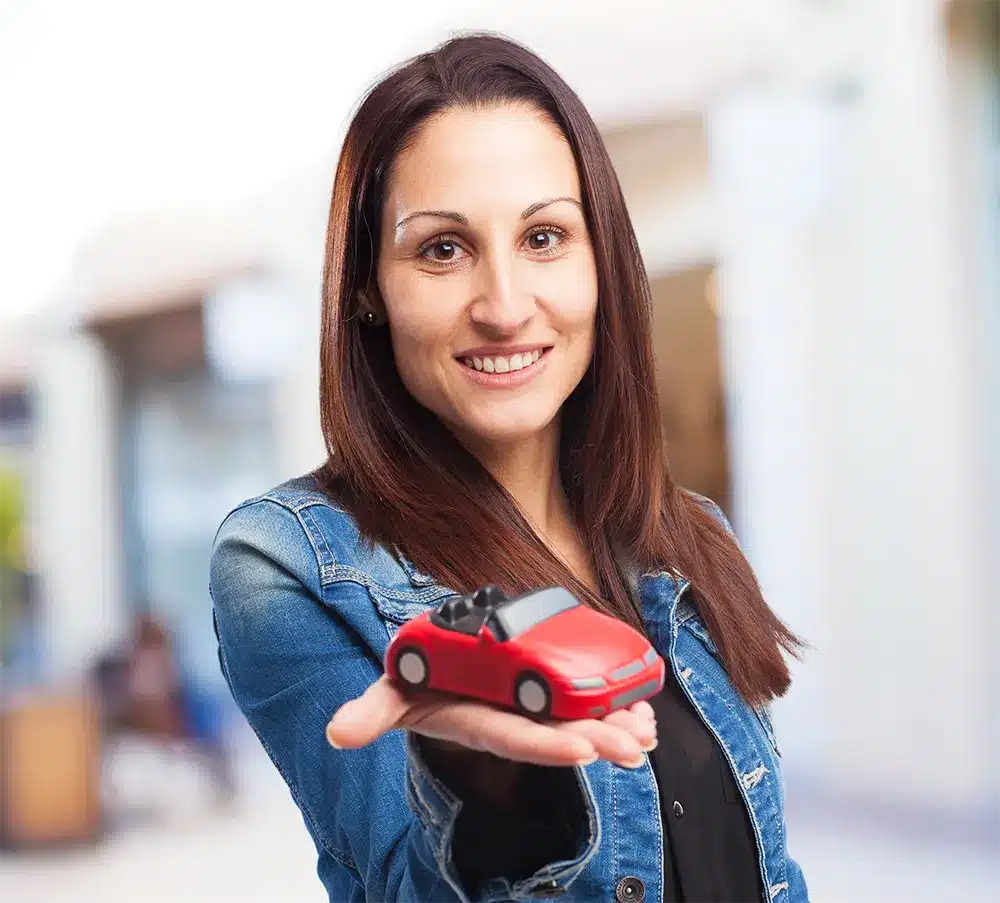 strip-img Smiling woman in a denim jacket holding a red toy car, representing vehicle-related services or legal claims.