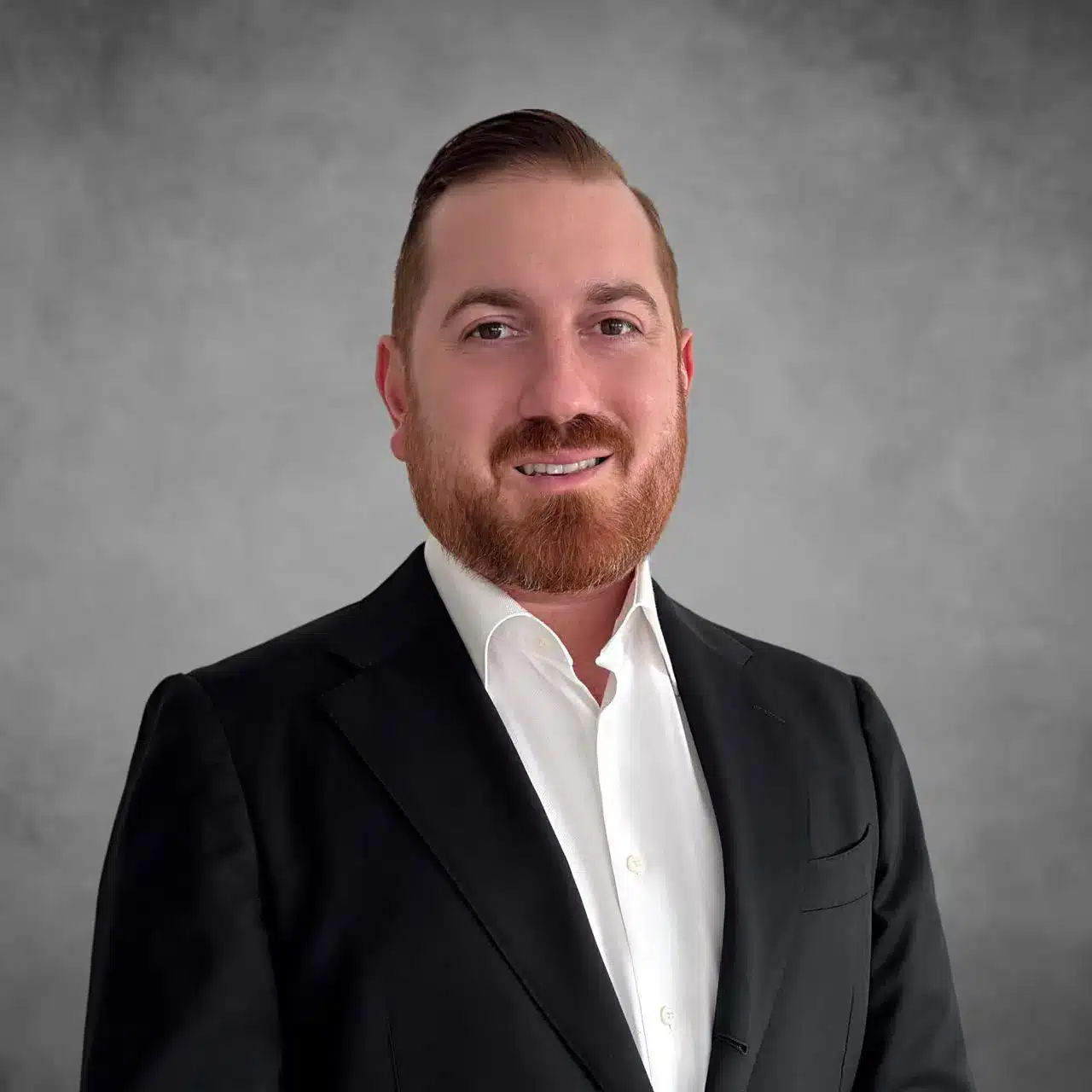 Novaj Javidzad, Chief Strategy Officer, smiling in a professional headshot with a gray background, wearing a black suit and white shirt.