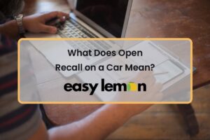 Person checking an open vehicle recall on a laptop while reviewing documents, illustrating what an open recall on a car means